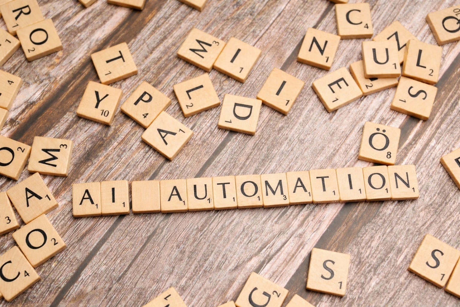 Scrabble tiles spelling AI AUTOMATION on a wooden surface. Photo by Markus Winkler on Unsplash.