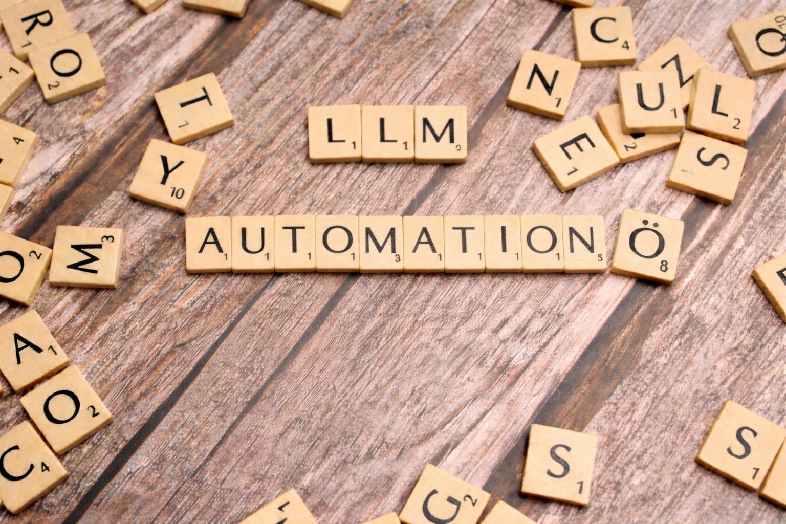 Scrabble tiles spelling LLM and AUTOMATION on a wooden surface. Photo by Markus Winkler on Unsplash.